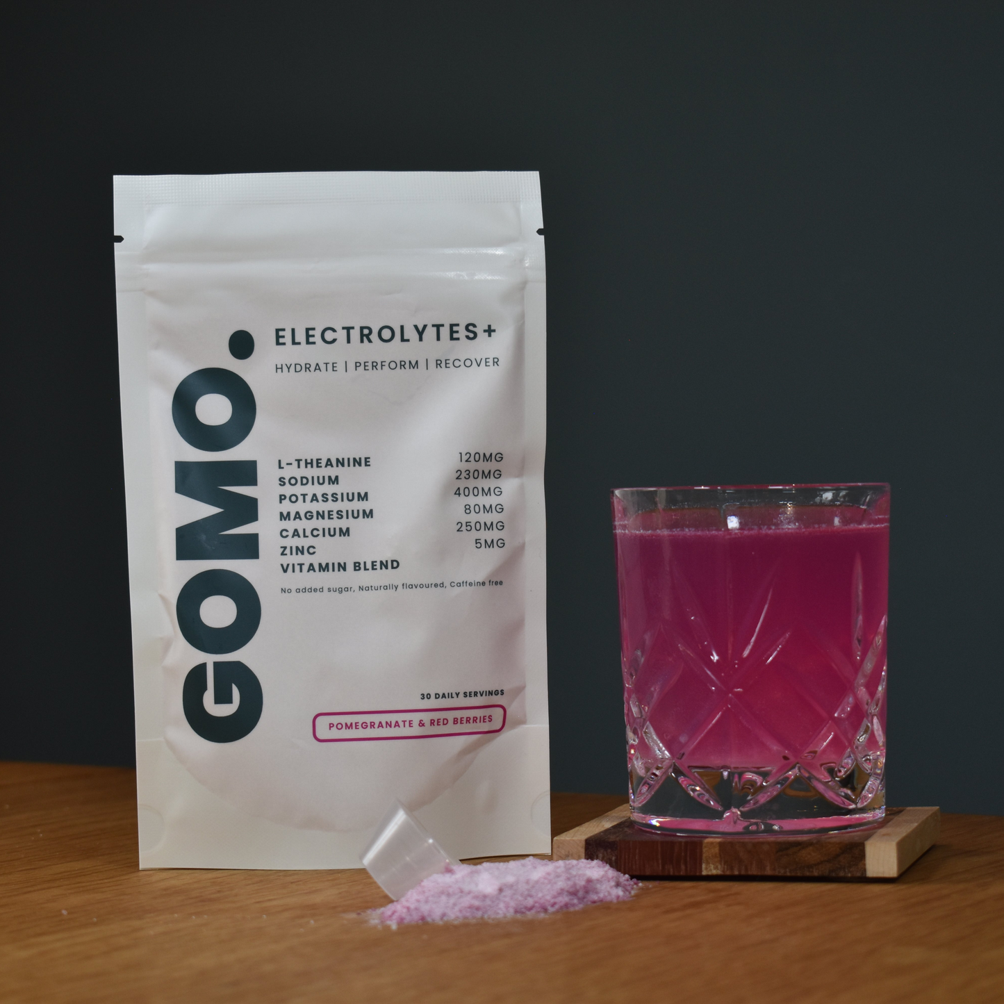 GOMO electrolytes+ pouch with a glass of pink drink on a wooden surface